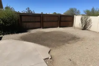 Leveled dirt patch after cactus stump removal between a concrete patio and wooden fence in Phoenix, AZ.
