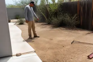 Technician with a rake and broom inspecting cleared desert soil in a Phoenix, AZ yard.