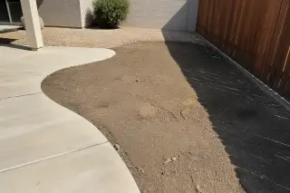 Disturbed soil and rake marks in a Phoenix, AZ yard between a concrete patio and a wooden fence.