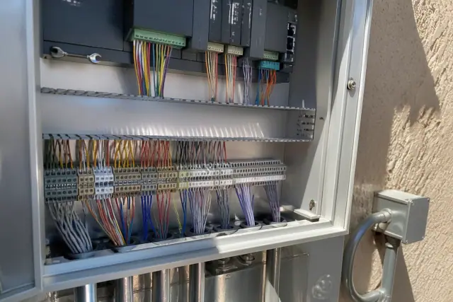Technician wiring a building automation control cabinet in Mesa, AZ, showing color-coded cables and terminal blocks.