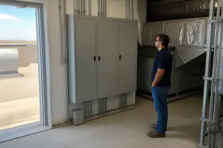 Technician observing a closed automation cabinet and overhead cooling ducts in a Phoenix, AZ mechanical room.