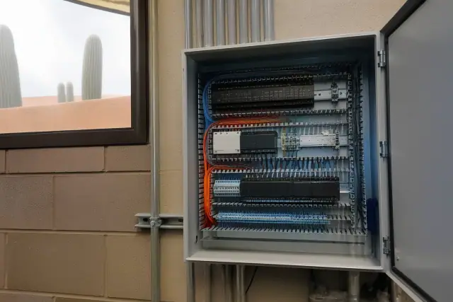 Open control cabinet with color-coded wiring in a Phoenix, AZ building, featuring a warehouse view with cacti.