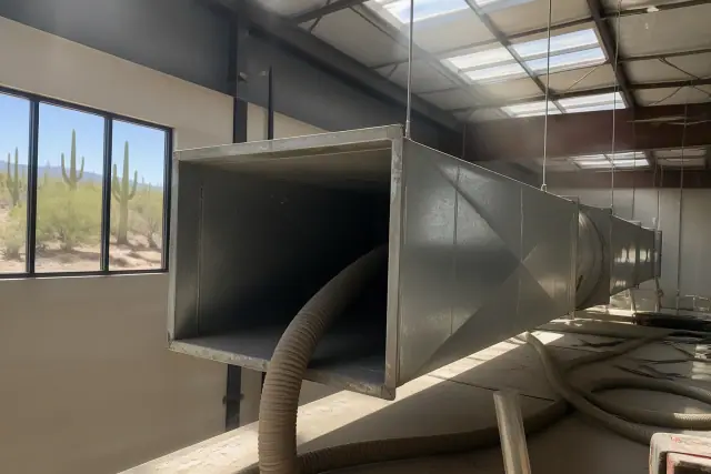 Commercial ductwork cleaning with vacuum hoses in a Phoenix, AZ industrial warehouse with desert sunbeams.