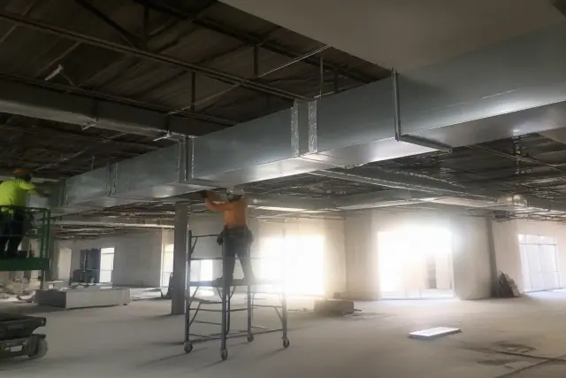 Sheet metal workers installing galvanized steel ductwork on a ceiling in a commercial building in Peoria, AZ.