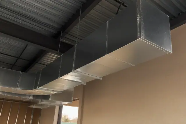 Galvanized steel ductwork installation in a Tempe, AZ commercial building with desert sunlight on a stucco wall.