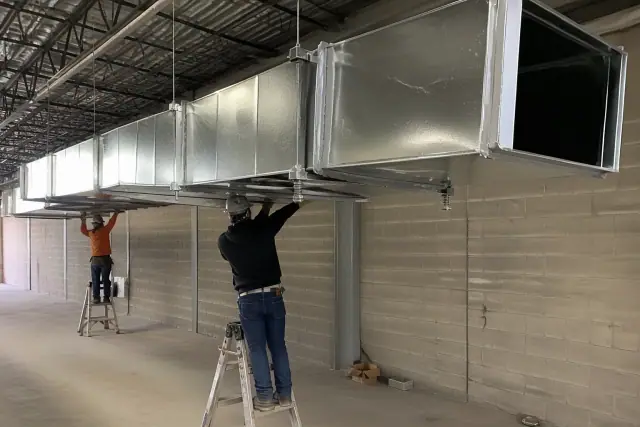Galvanized steel ductwork installation with mastic tape and vibration hangers in a Phoenix, AZ warehouse.