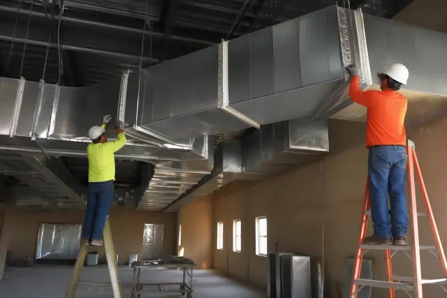 Sheet metal workers installing galvanized steel ductwork on a ceiling at a commercial job site in Phoenix, AZ.