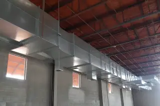 Galvanized steel ductwork suspended from a warehouse ceiling with exposed concrete walls in Phoenix, AZ.