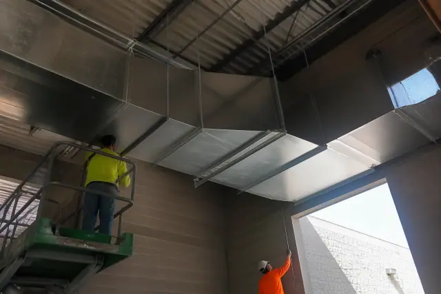 Sheet metal workers installing galvanized steel HVAC ductwork in a Phoenix, AZ industrial warehouse.