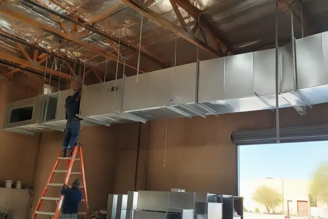 Sheet metal workers installing galvanized steel ductwork on a warehouse ceiling in Scottsdale, AZ.