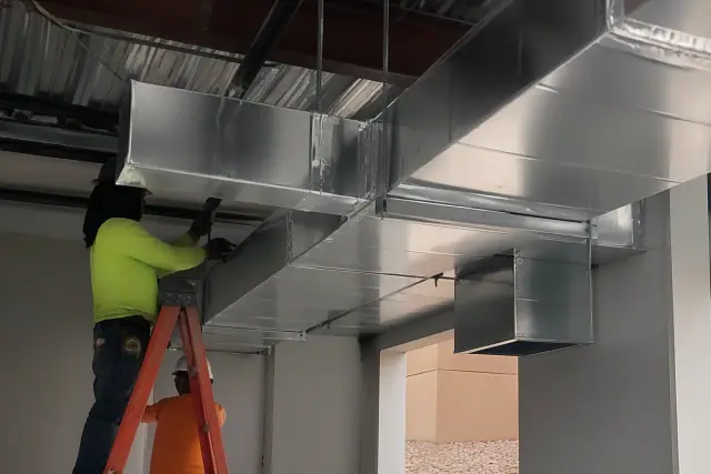 Contractors installing galvanized steel HVAC ductwork from an industrial ceiling in Chandler, AZ.