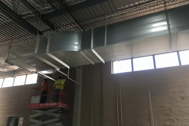 Sheet metal workers installing galvanized steel HVAC ductwork in an industrial warehouse in Avondale, AZ.