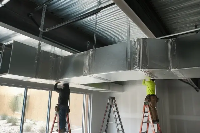 Contractors installing galvanized steel ductwork from an industrial ceiling at a jobsite in Glendale, AZ.