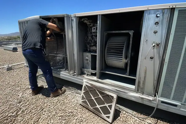 HVAC technician performing a rooftop unit tune-up on a gravel roof in Scottsdale, AZ.