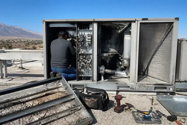 Technician performing a seasonal HVAC rooftop unit tune-up on a gravel roof in Goodyear, AZ.