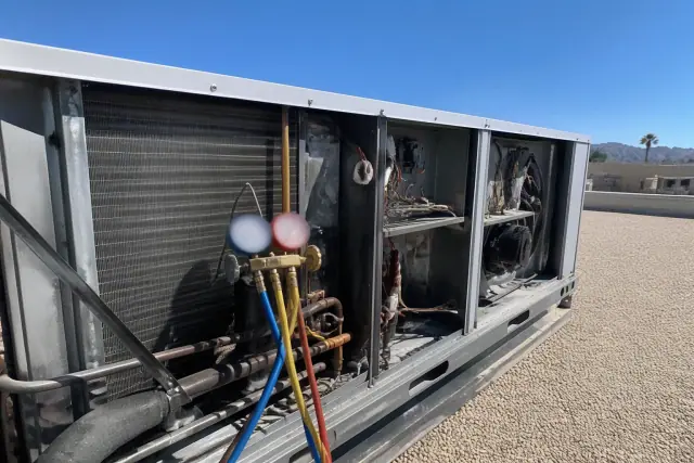 Manifold gauges connected to an open rooftop HVAC unit on a gravel roof in Scottsdale, AZ.