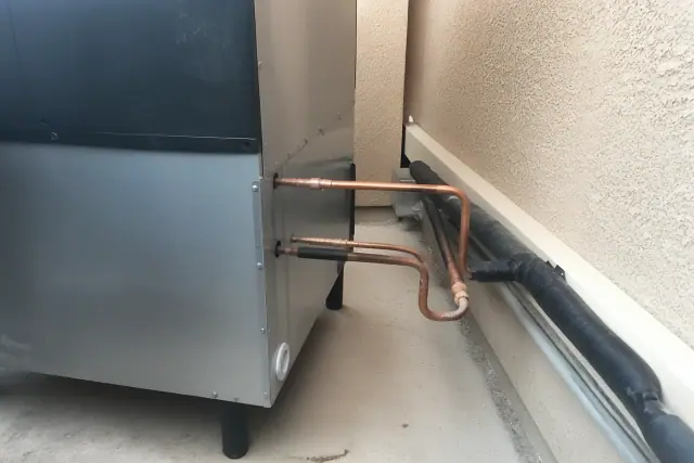 Commercial ice machine installed with copper refrigerant lines and insulation against a stucco wall in Phoenix, AZ.