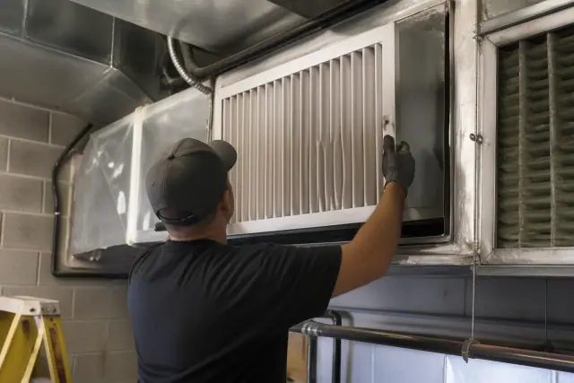 Contractor installing a commercial air purification unit into ductwork in a Tempe, AZ building.