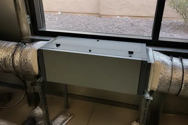 Technician installing a commercial air purification unit into ductwork at a jobsite in Mesa, AZ.