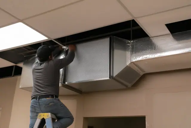 Installer securing a commercial air purification unit into metal ductwork in Chandler, AZ.