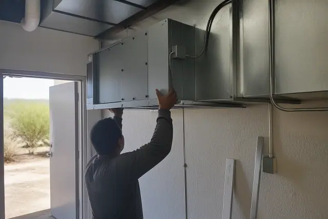 A contractor installing a commercial air purification unit into ductwork in a mechanical room in Surprise, AZ.
