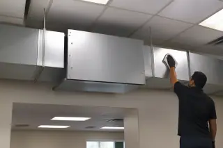 Technician wiping down a commercial air purification unit on ductwork near ceiling tiles in Phoenix, AZ.