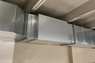 Commercial air purification unit secured to supply ductwork with concrete ceiling beams in Phoenix, AZ.