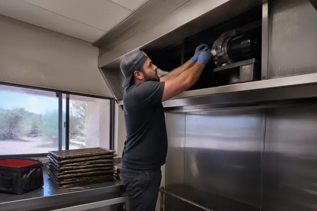 Technician inspecting a commercial kitchen exhaust hood and grease filters at a job site in Phoenix, AZ.