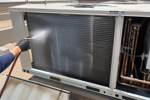 Technician cleaning condenser coils on a commercial rooftop unit in Phoenix, AZ.