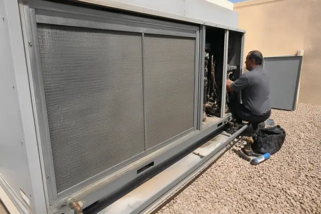 Technician performing a seasonal tune-up on a dusty commercial rooftop AC unit in Phoenix, AZ.