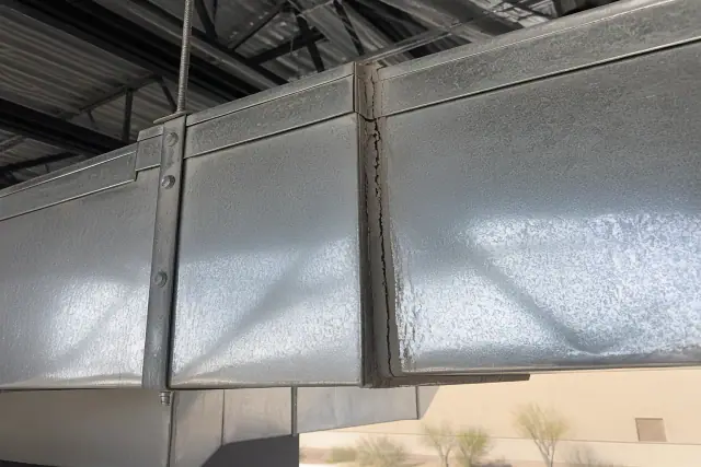 Cracked grey sealant at a galvanized steel duct joint in a commercial building in Phoenix, AZ.