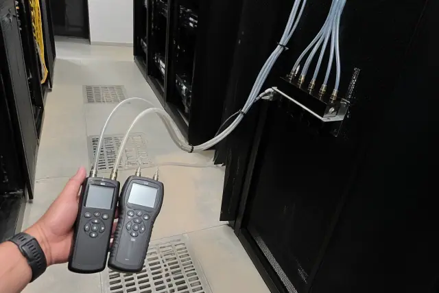 Handheld air quality sensor testing in a Phoenix, AZ server room with dust on the floor and drainage covers.