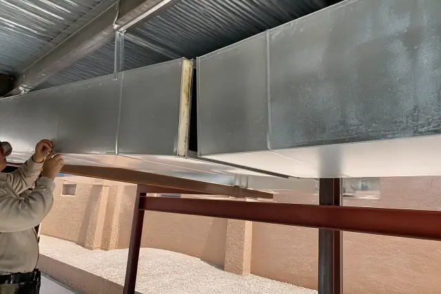 Sheet metal workers installing galvanized steel ductwork with a visible unsealed joint at a jobsite in Phoenix, AZ.