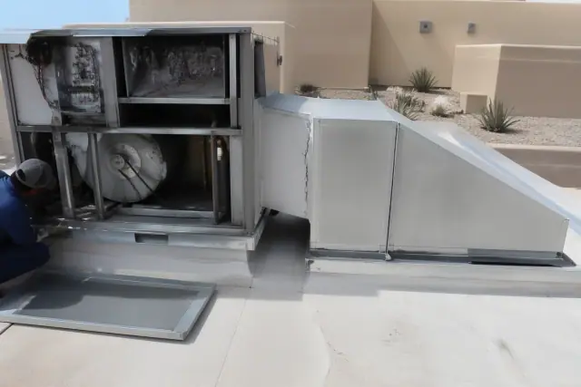 Worker performing a seasonal tune-up on a rooftop unit with sealant degradation in Phoenix, AZ.