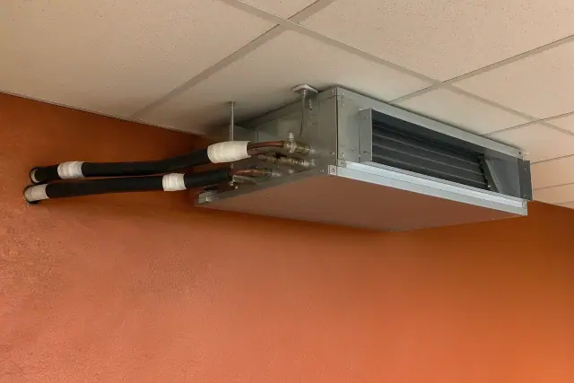 Ceiling-mounted VRF unit with insulated copper refrigerant lines on a stucco wall in Phoenix, AZ.