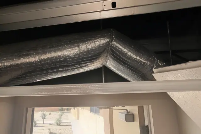 Kinked flexible duct with a sharp 90-degree crush restricting airflow above a drop ceiling in Phoenix, AZ.