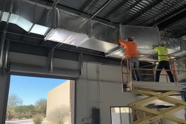 Sheet metal workers installing galvanized steel ductwork on a ceiling at a commercial site in Phoenix, AZ.