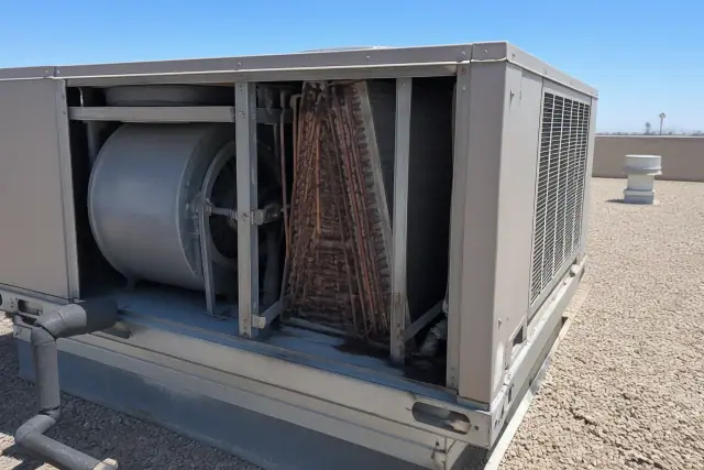 HVAC rooftop unit with internal blower and copper coils exposed during maintenance on a gravel roof in Phoenix, AZ.
