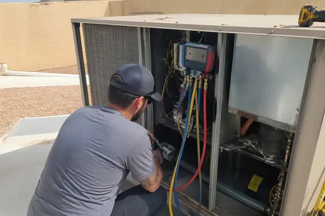 HVAC technician performing a seasonal rooftop unit tune-up with digital manifold gauges in Phoenix, AZ.
