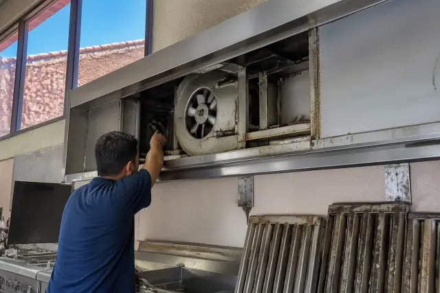 Contractor inspecting a commercial kitchen exhaust hood and motor in Phoenix, AZ.