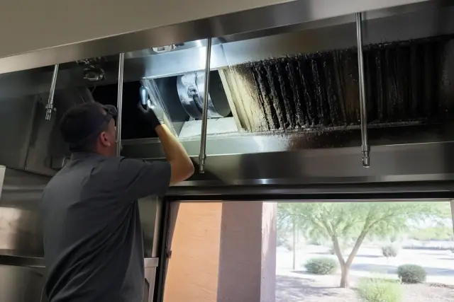 Technician inspecting a commercial kitchen exhaust hood with grease buildup in a Chandler, AZ restaurant.