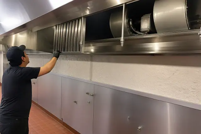 Technician inspecting a commercial kitchen grease filter and exhaust hood at a restaurant in Gilbert, AZ.