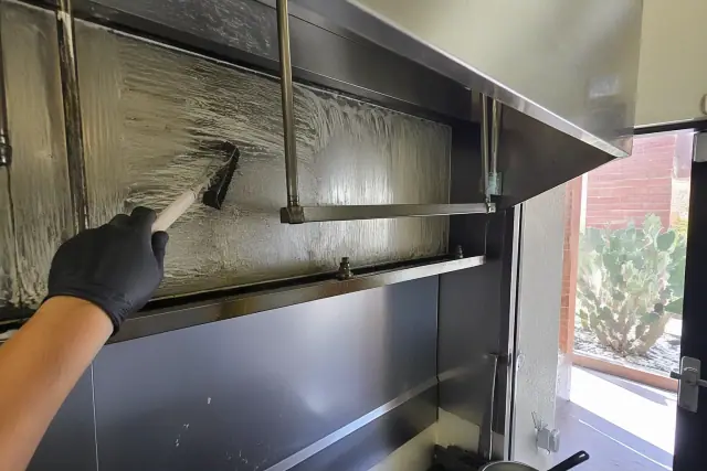 A technician cleaning a restaurant hood plenum in Glendale, AZ with a scrub brush and industrial degreaser.