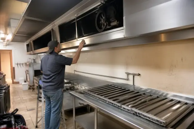 Contractor inspecting the interior motor and ventilation housing of a commercial kitchen hood in Tempe, AZ.