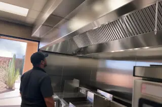Stainless steel kitchen exhaust hood with clean grease filters and a cactus visible through the window in Phoenix, AZ.