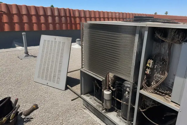 Technician performing a commercial HVAC rooftop unit tune-up on a gravel roof in Phoenix, AZ.