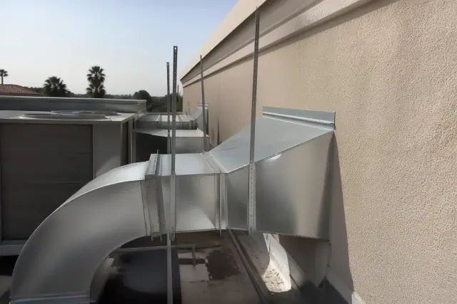 Galvanized steel transition boots and kitchen exhaust ductwork installed on a stucco wall at a Phoenix, AZ job site.
