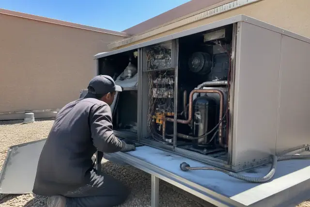 Contractor performing a seasonal tune-up on a small retail rooftop HVAC unit in Phoenix, AZ.