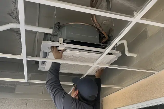 Technician installing a ceiling-cassette VRF unit in a drop ceiling during HVAC maintenance in Phoenix, AZ.