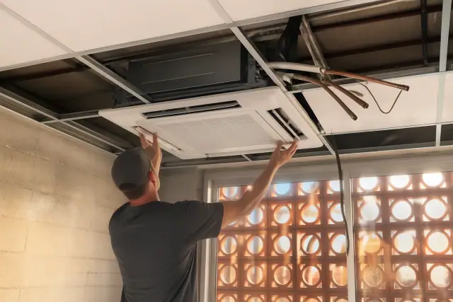 Technician installing a VRF ceiling unit in a Scottsdale, AZ commercial space with exposed refrigerant piping.